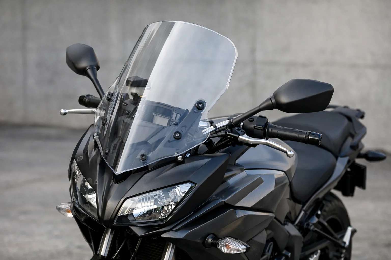 Bulle transparente montée devant le poste de pilotage d’une moto stationnée.