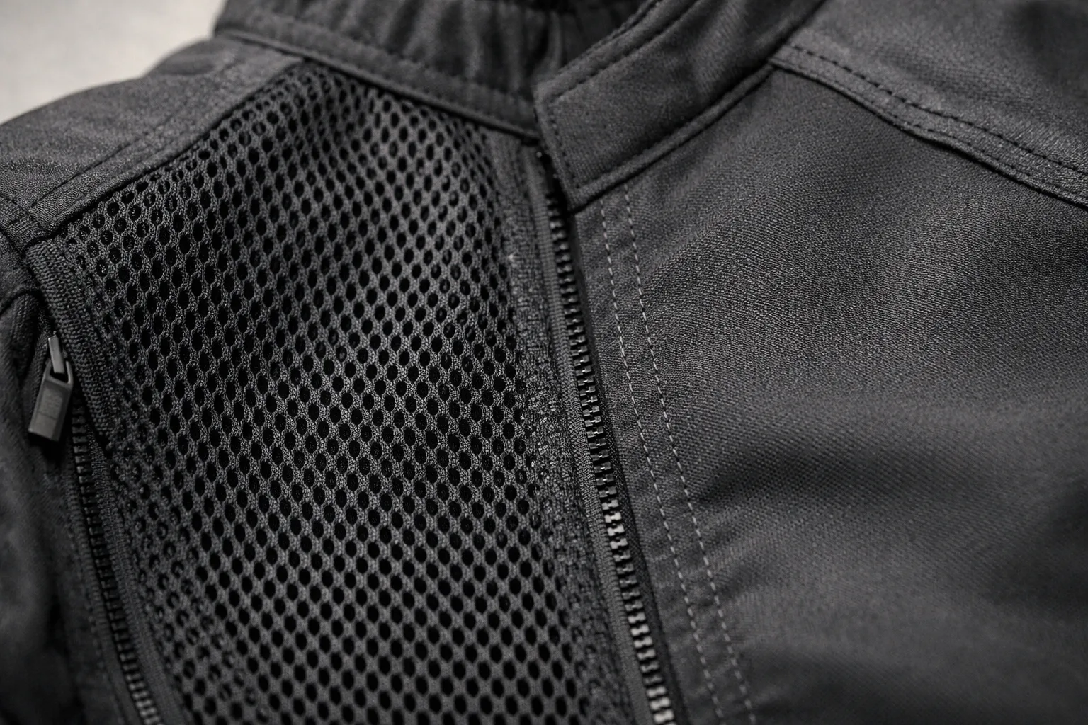 Détail d’une veste moto montrant côte à côte un panneau en maille ajourée et une zone en textile plein.