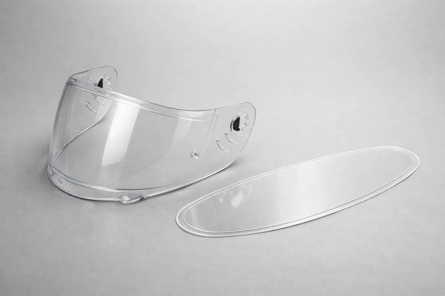 Une visière de casque moto transparente et un insert antibuée amovible posés côte à côte.