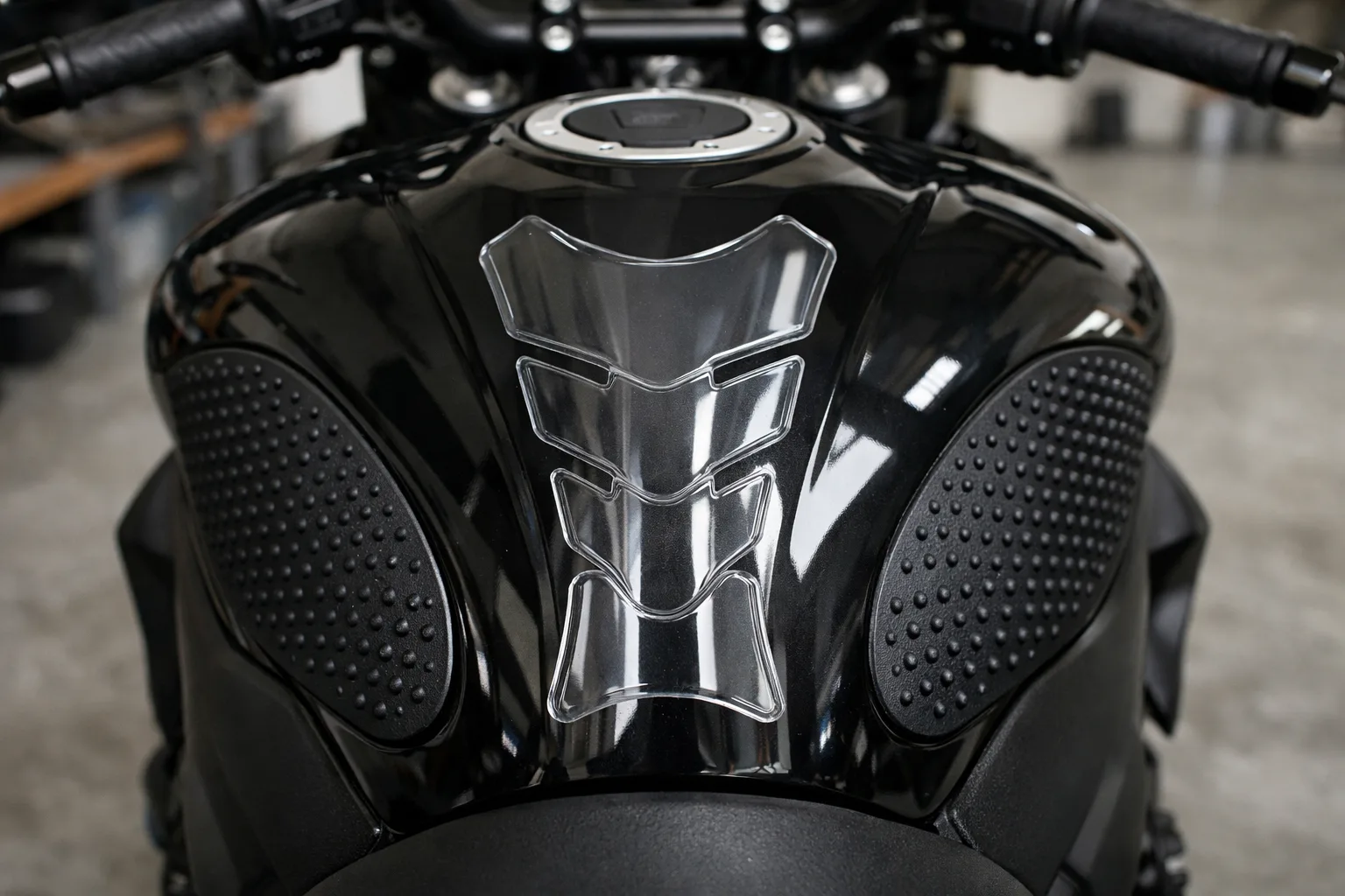 Réservoir de moto équipé d’une protection centrale transparente et de grips latéraux noirs.