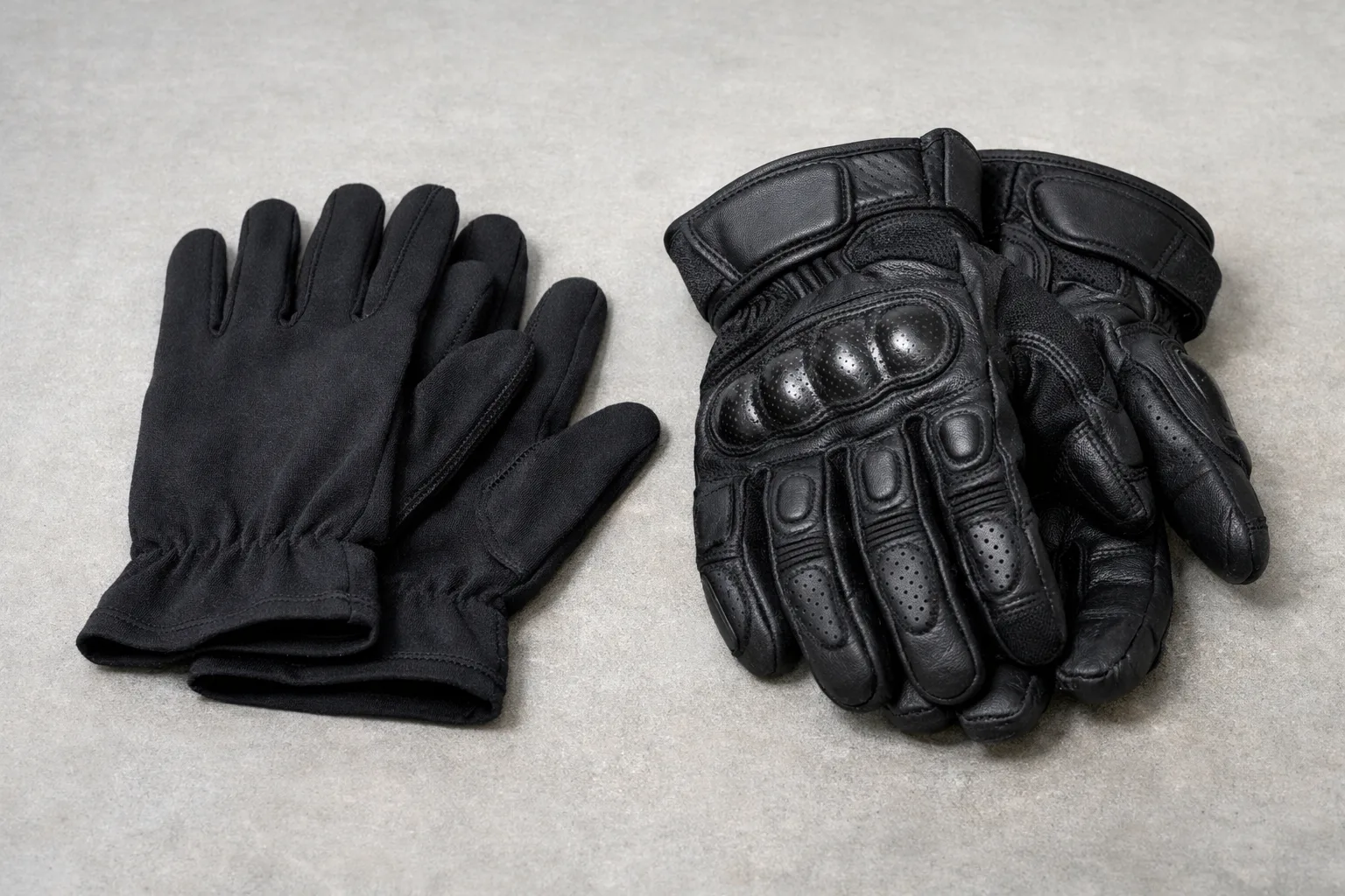 Une paire de sous-gants fins posée à côté de gants de moto noirs.