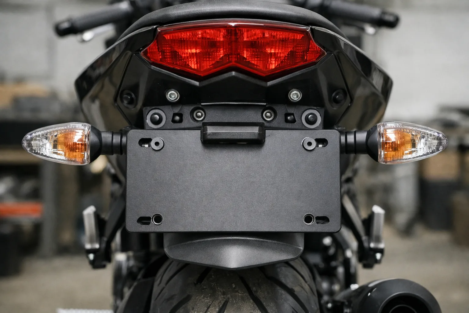 Support de plaque monté sous le feu arrière d’une moto, près des clignotants et du garde-boue.
